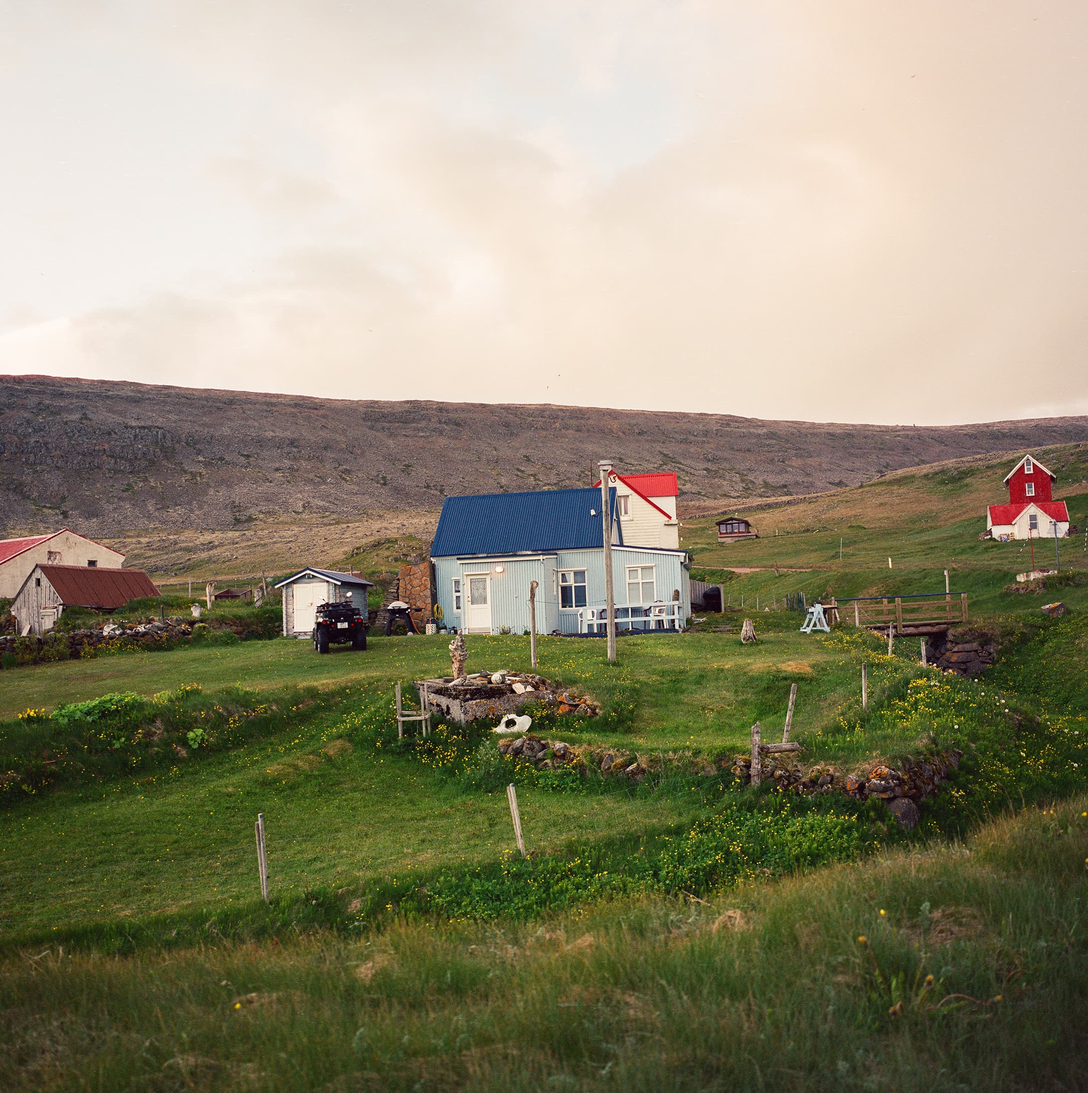 A small cluster of colorful Icelandic farm buildings on a green hillside above the sea