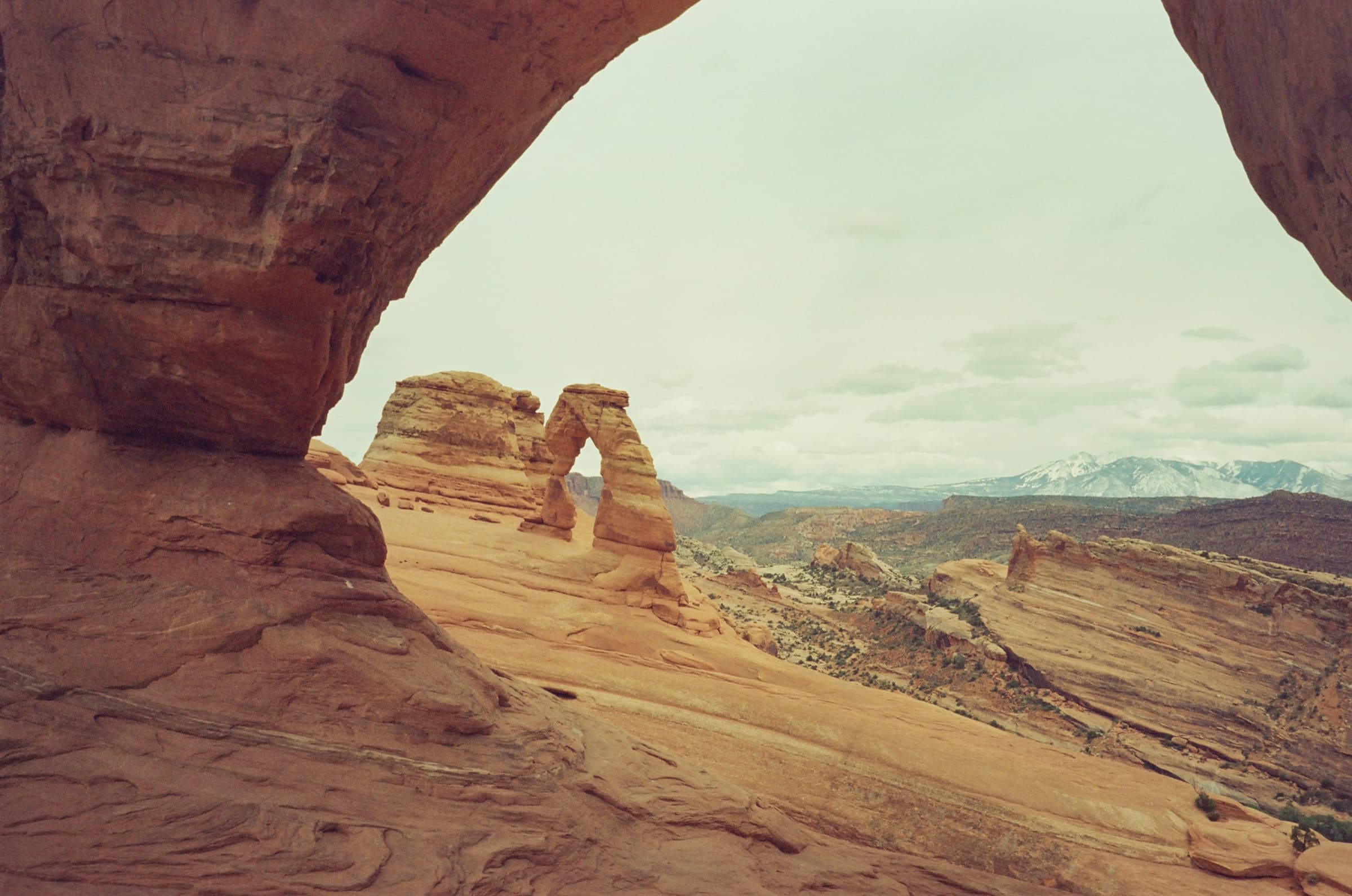 Delicate Arch framed through a sandstone window with the snow-capped La Sal Mountains in the distance