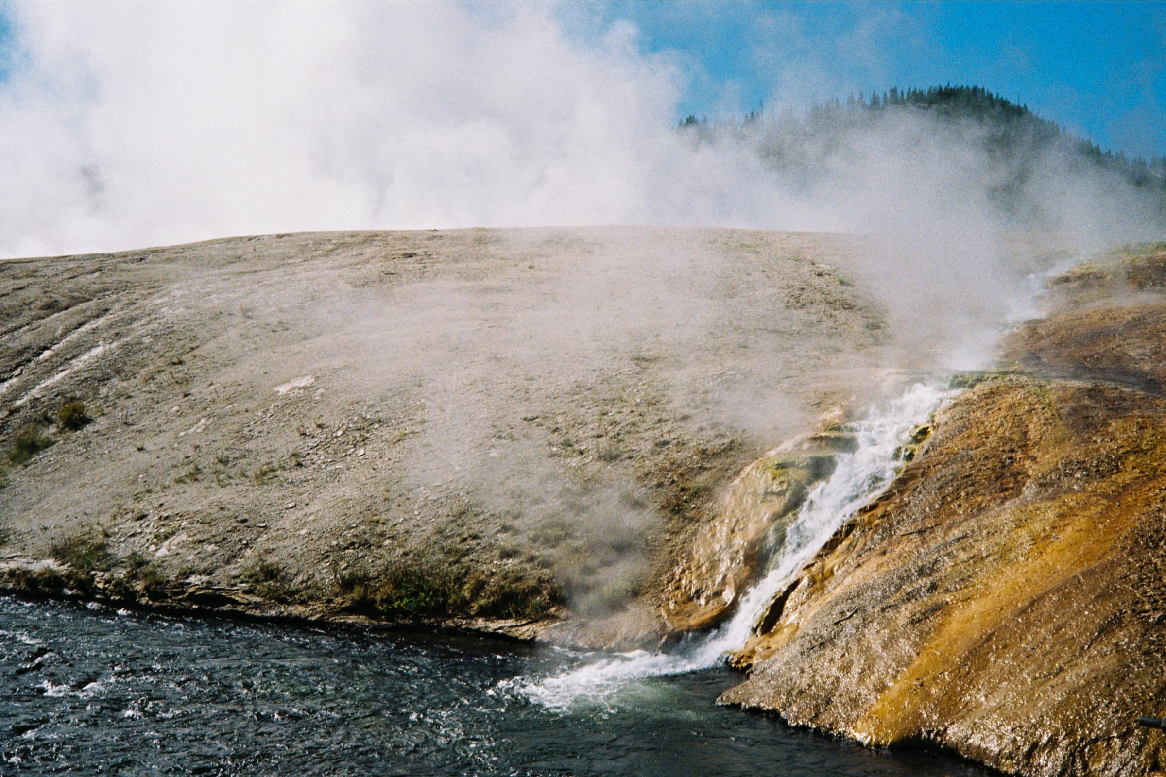Geothermal steam billowing above the Firehole River as it rushes over mineral-stained rocks