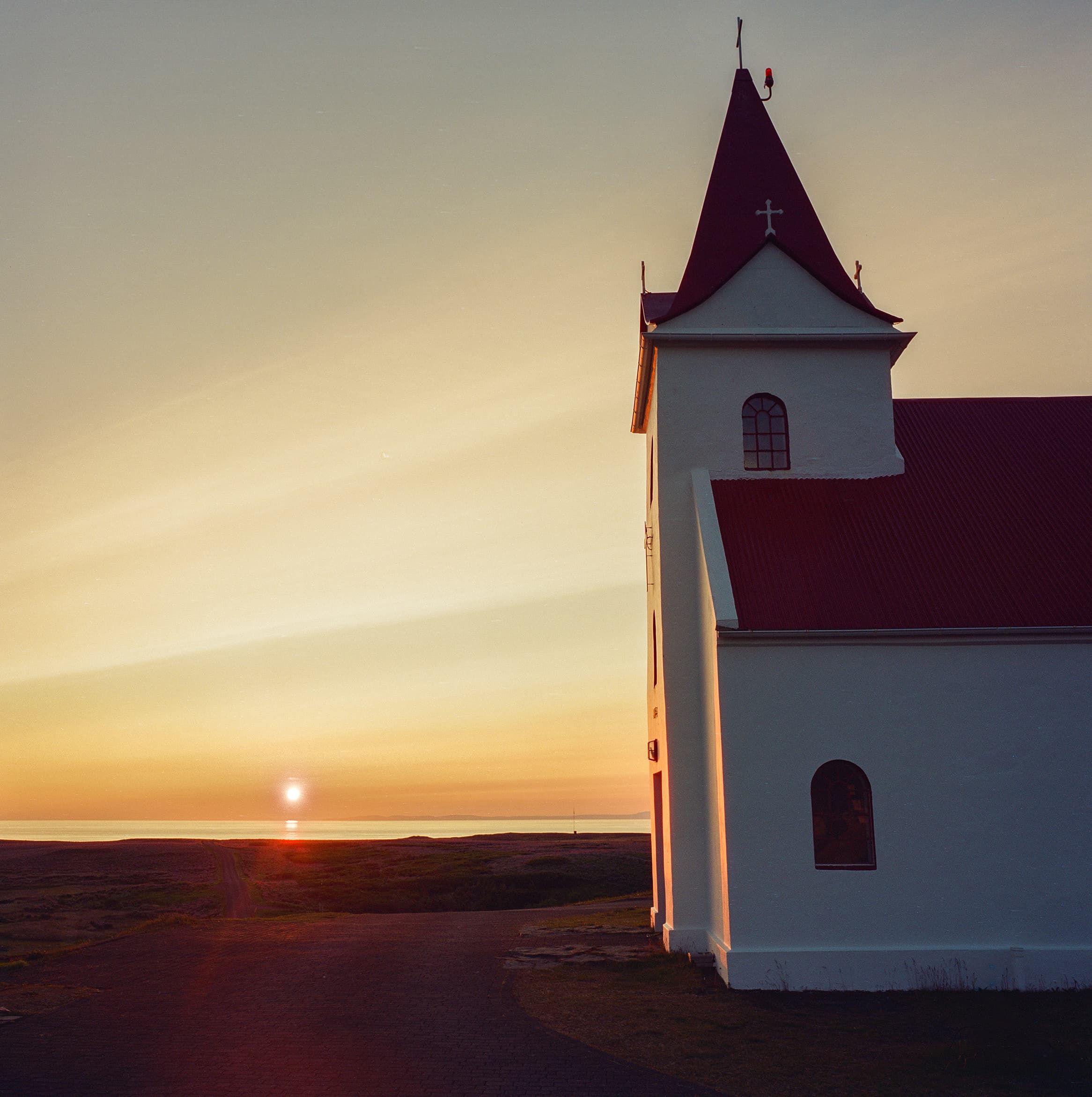 Ingjaldshóll Church bathed in golden midnight sun with rays of light radiating across the sky