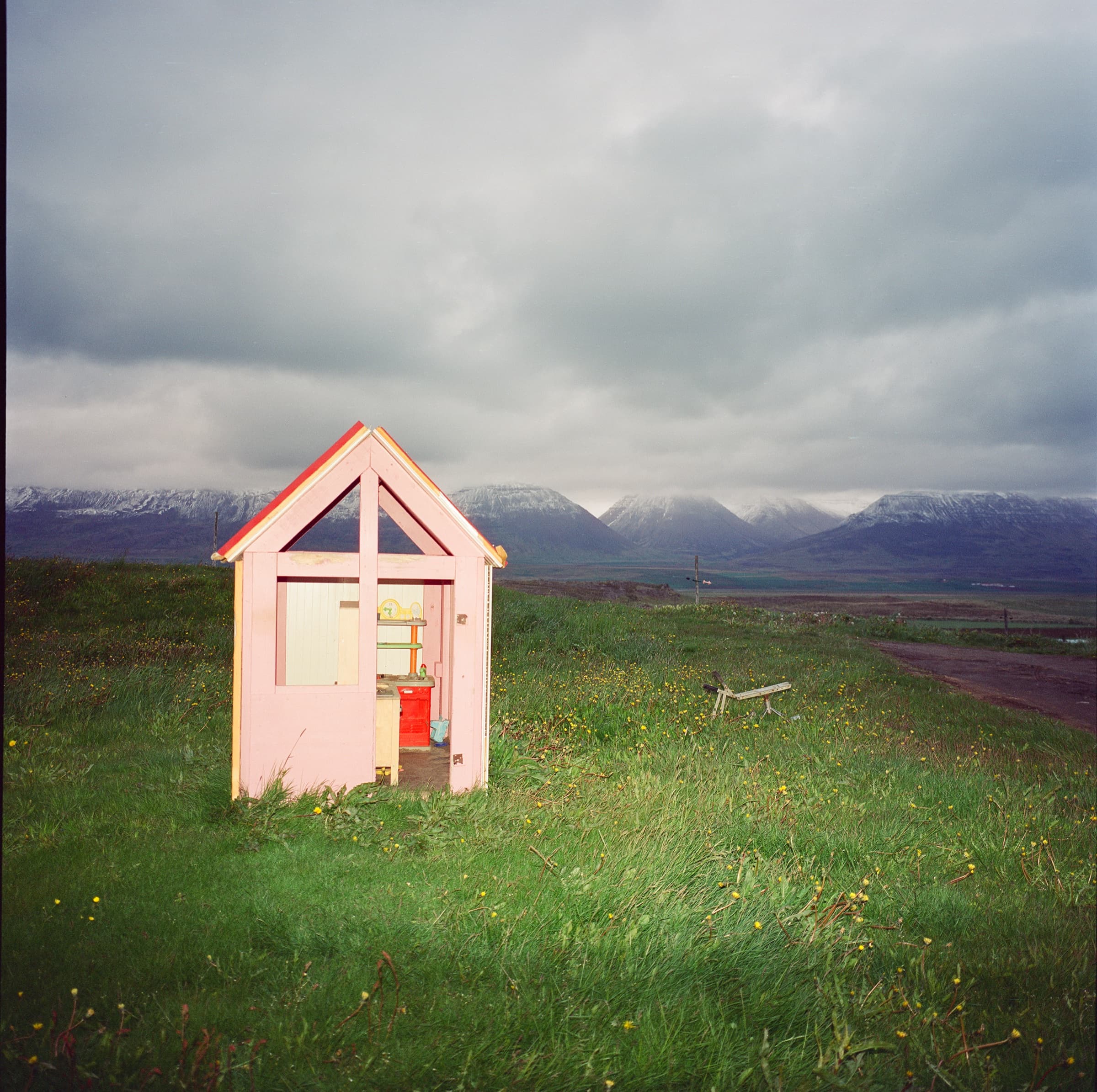 A small pink cabin sitting alone in a green wildflower meadow under a brooding overcast sky