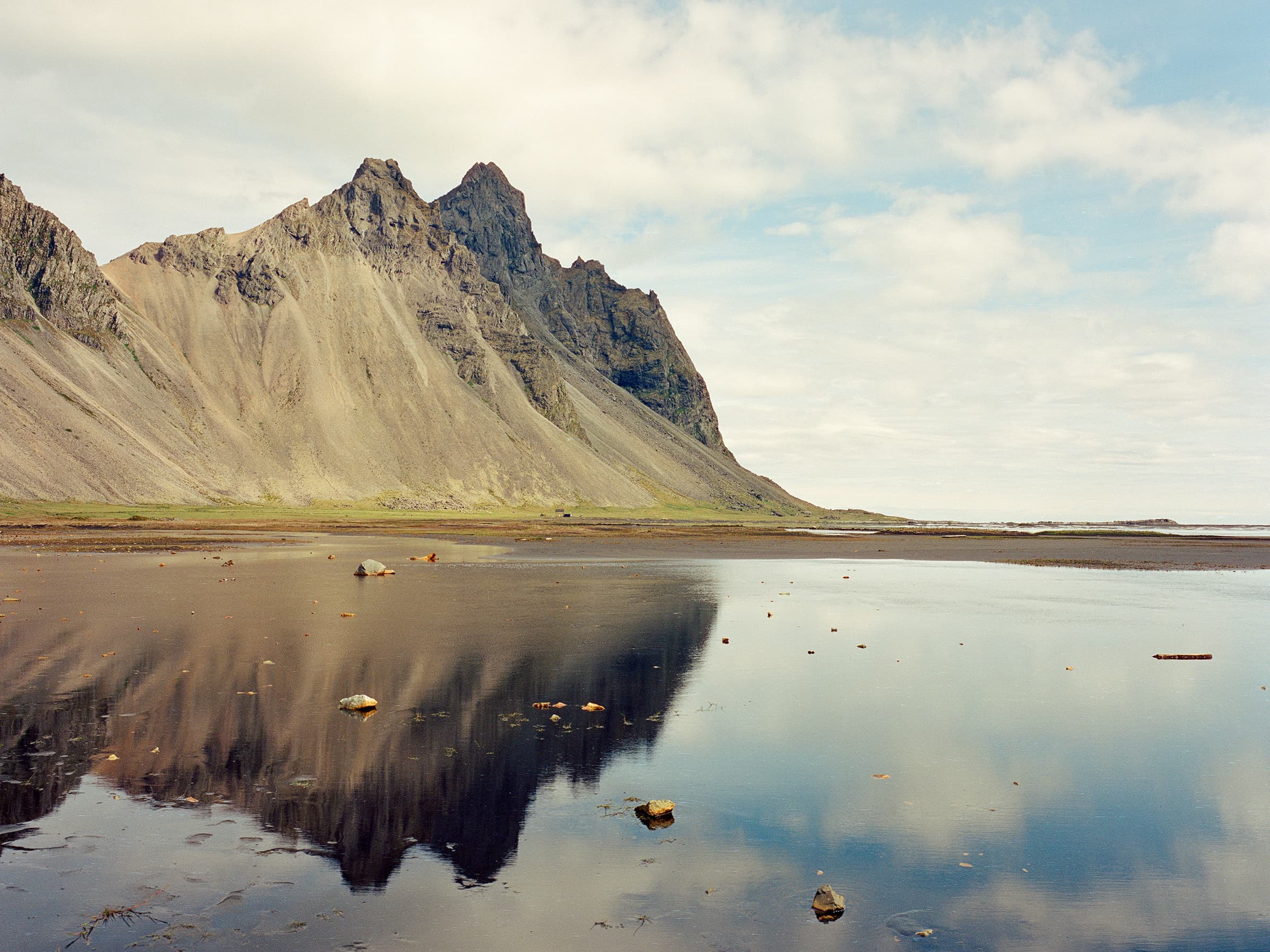 Vestrahorn mountain rising sharply above the black sand beach and its perfect mirror reflection below